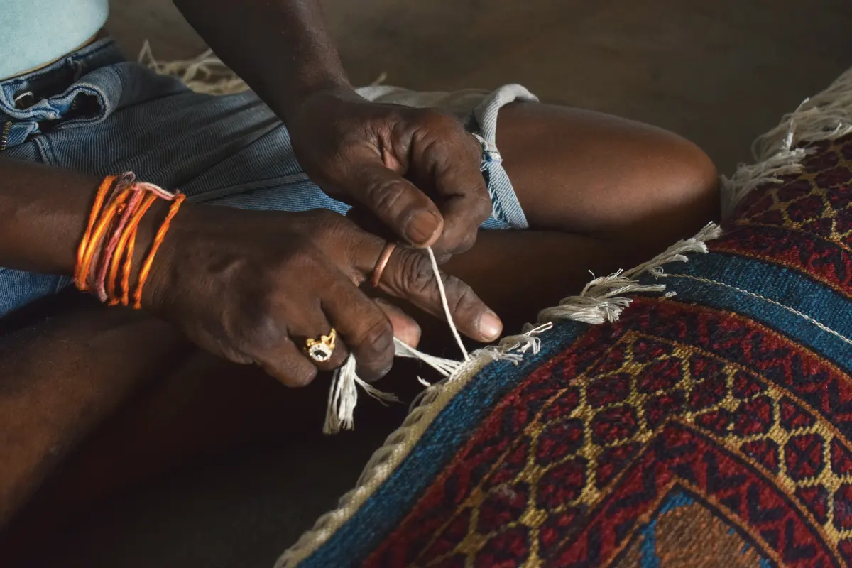 Hands tying the fringe of a handwoven rug