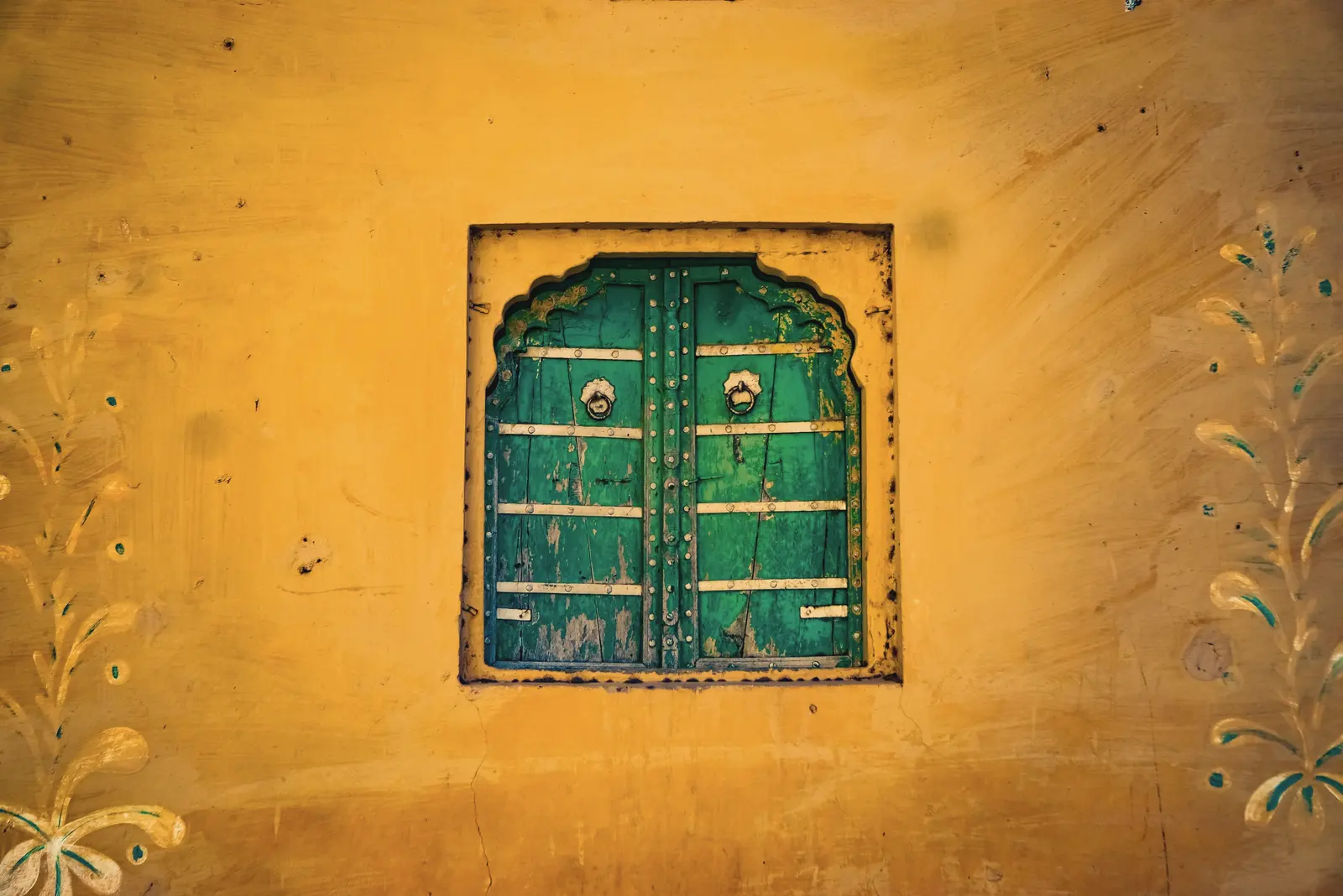 A small green wooden window set in a sunlit ochre wall
