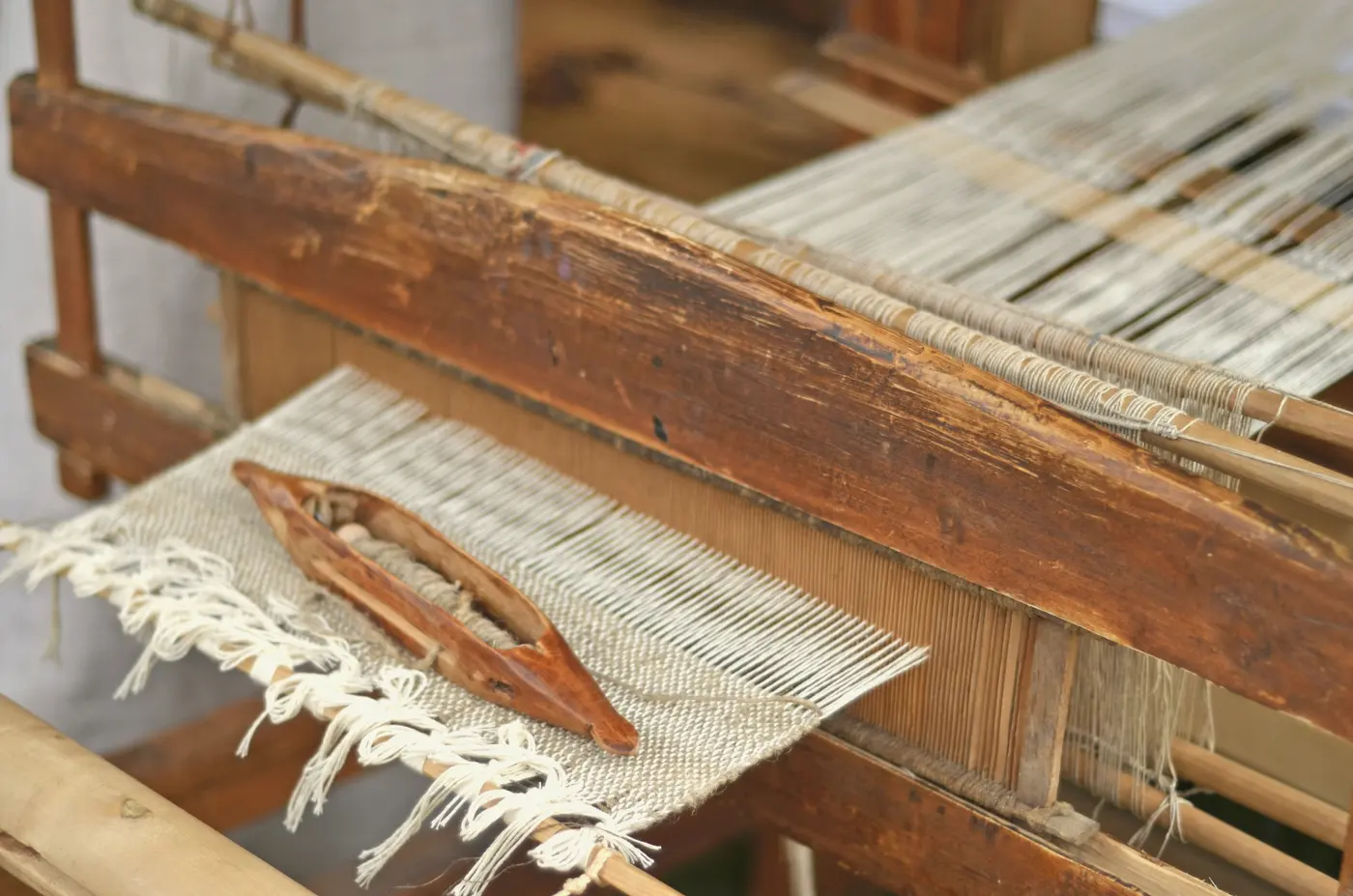 A wooden shuttle resting on half-woven white cotton on a loom