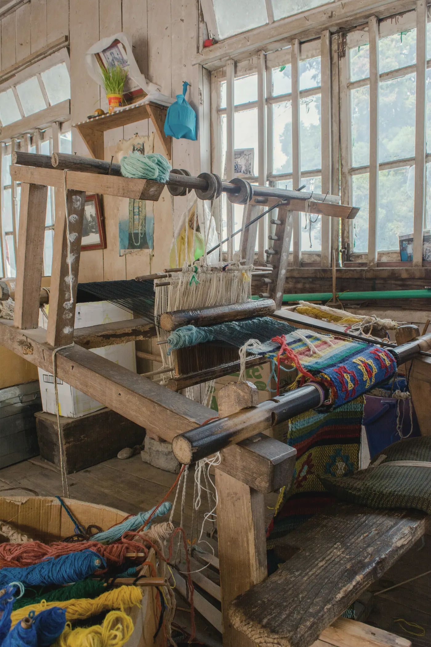 A wooden handloom in a sunlit workshop, colourful striped cloth half woven