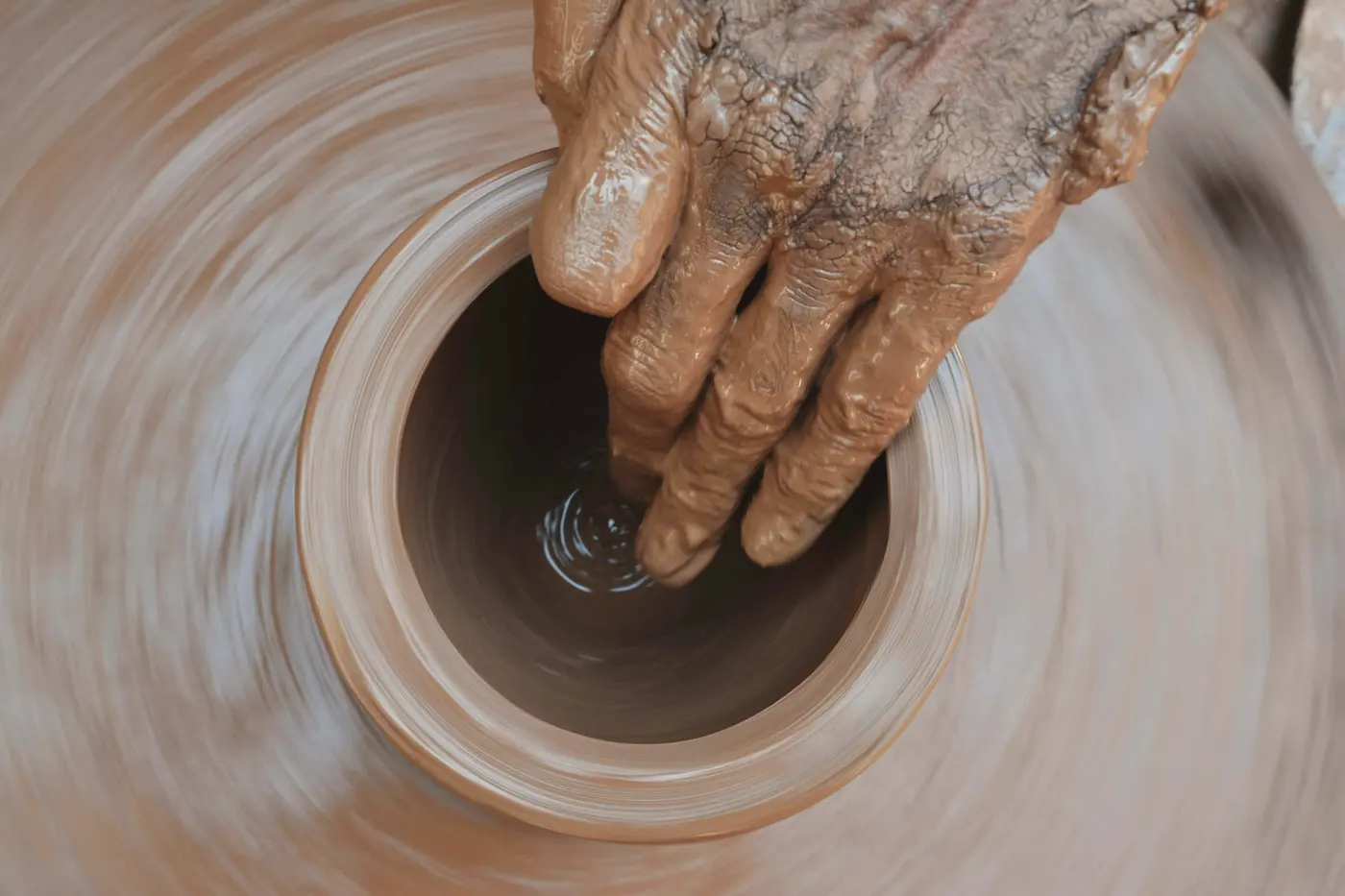 A potter's clay-covered hands shaping a pot on a spinning wheel