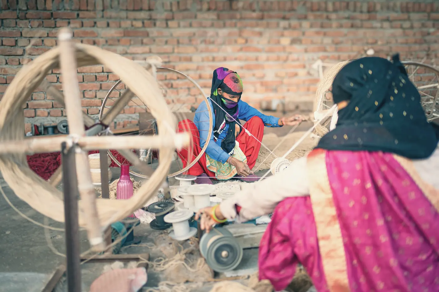 Women spinning yarn on a large wooden wheel outdoors